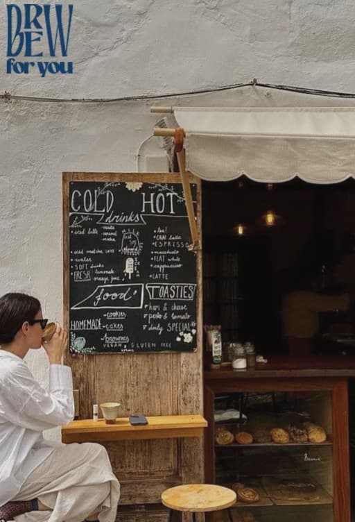 A customer sipping coffee outside the café, beneath its chalkboard menu