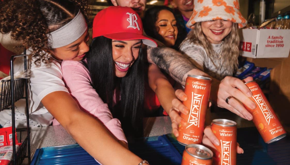 Friends reaching across a table to toast with cans of Nektar