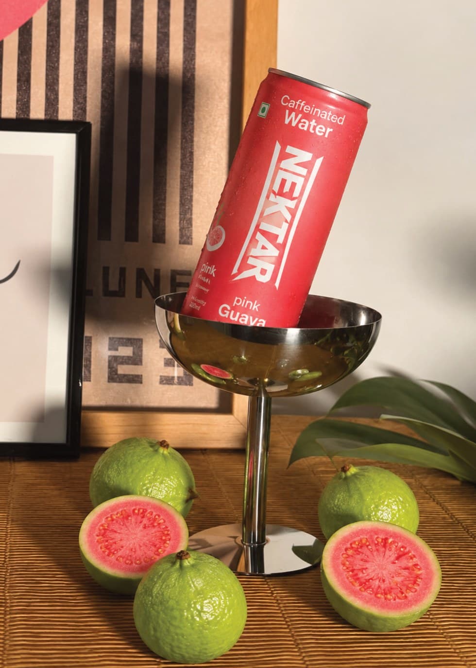 A can of Nektar pink guava tipped into a steel coupe beside halved guavas