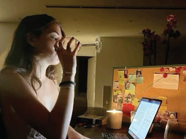 A woman drinking from a can at her desk late at night, laptop open