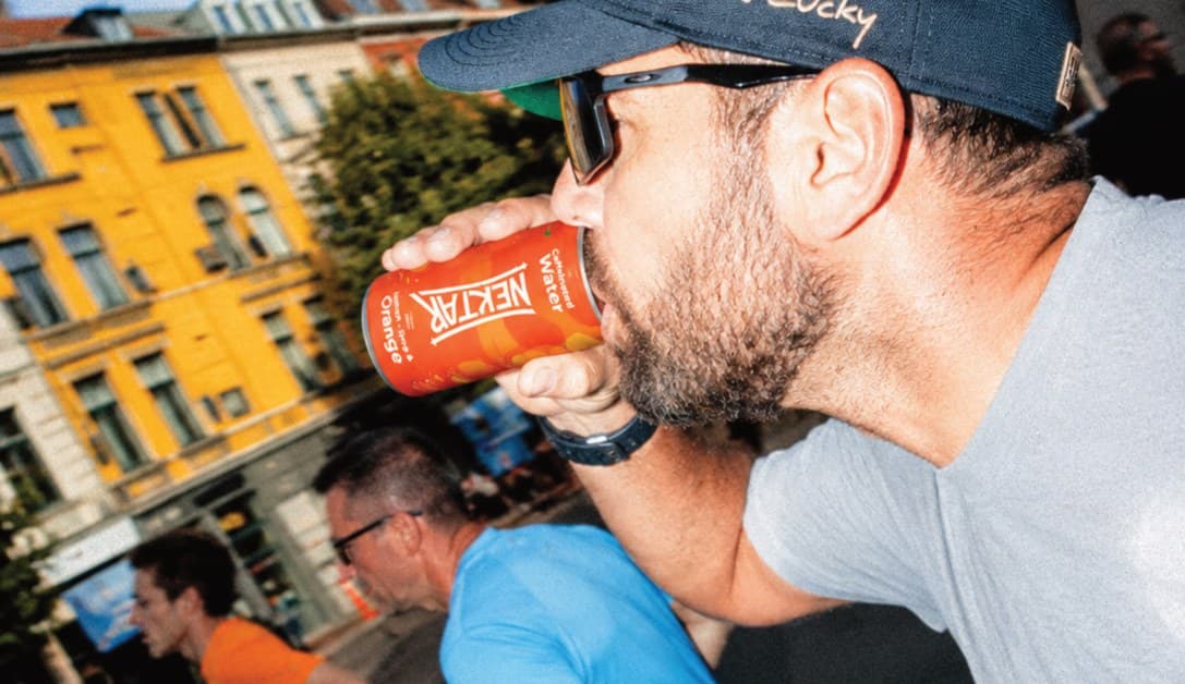 A man in a cap drinking from a can of Nektar on a city street