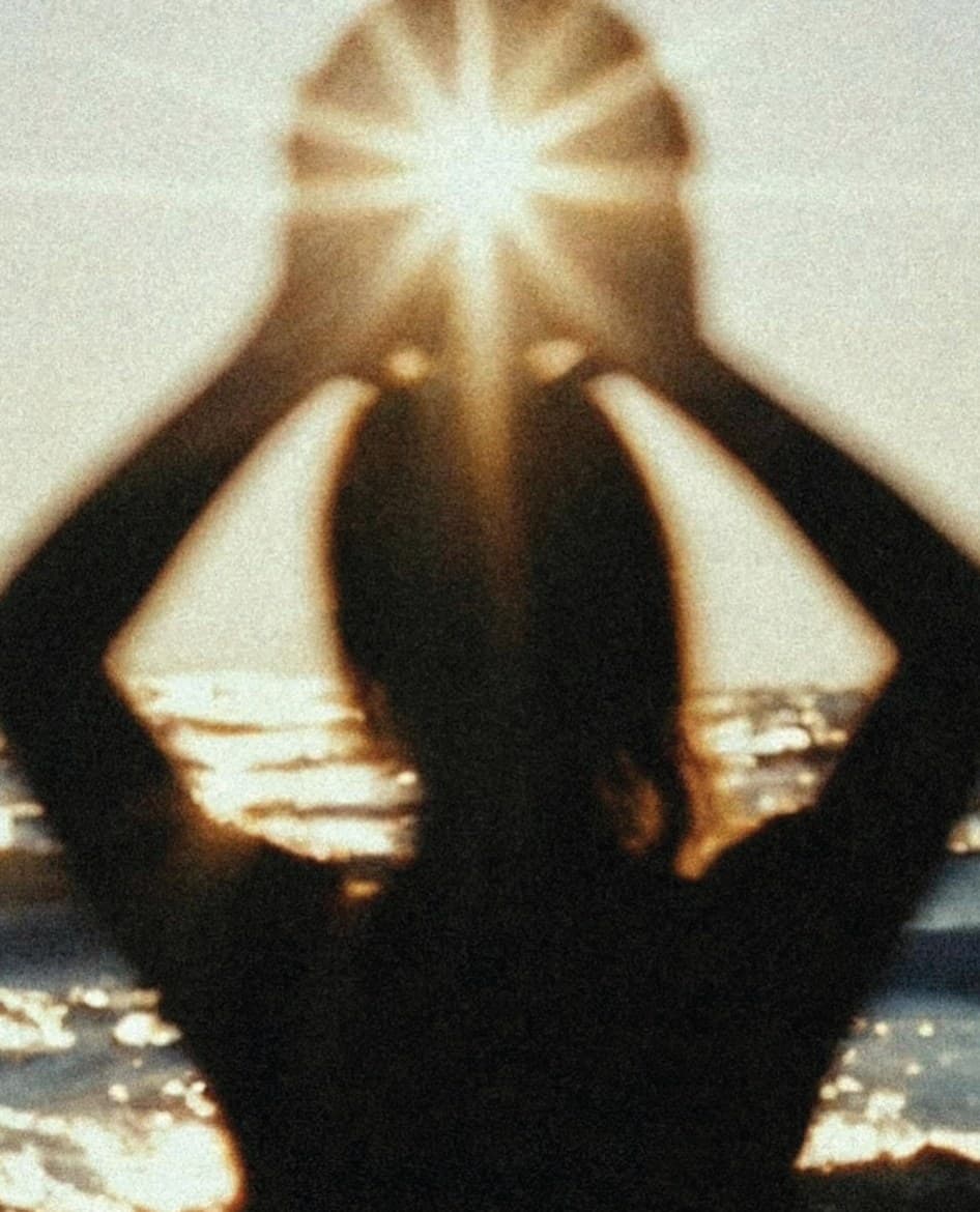 A silhouette holding the sun between their hands over the sea
