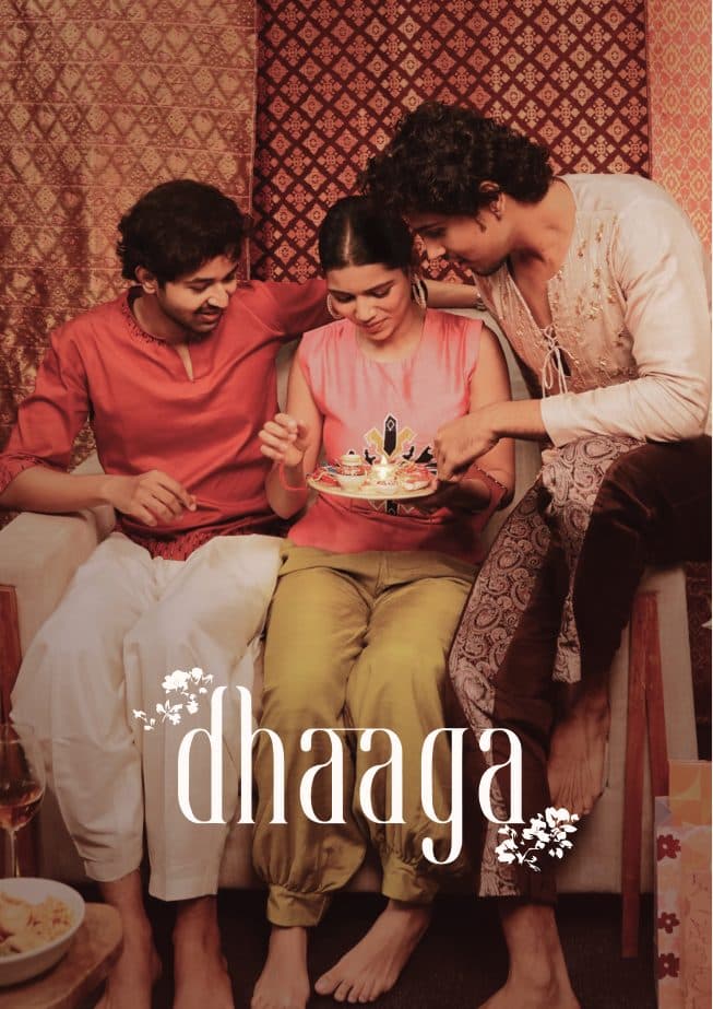 Three friends around a plate of sweets, under the Dhaaga wordmark