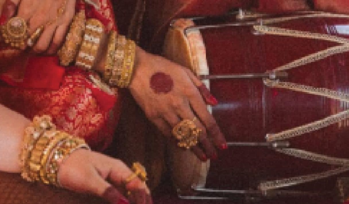 Hands in gold bangles and rings resting on a dhol