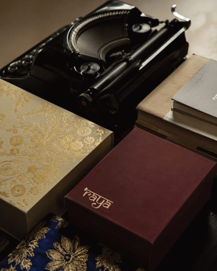 Gold and maroon Raya gift boxes beside a vintage typewriter