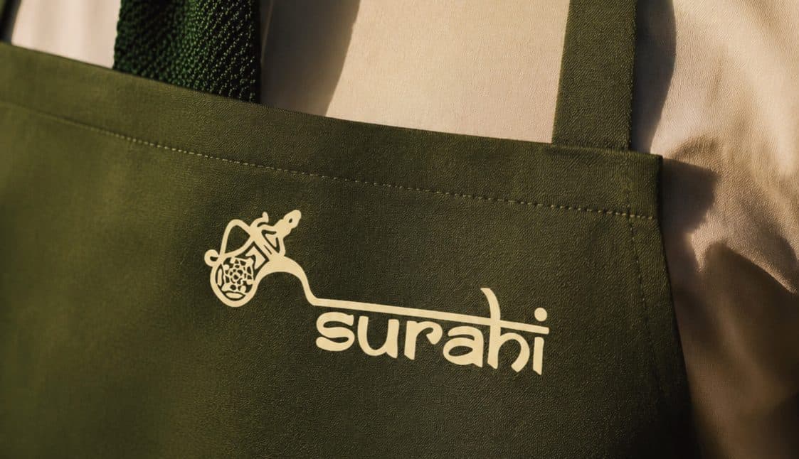 An olive apron embroidered with the Surahi logo