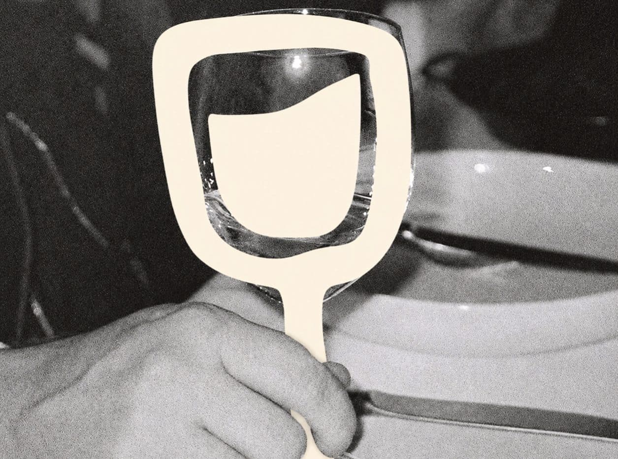 A black-and-white photo of a hand at the table, with a wine glass picked out in cream
