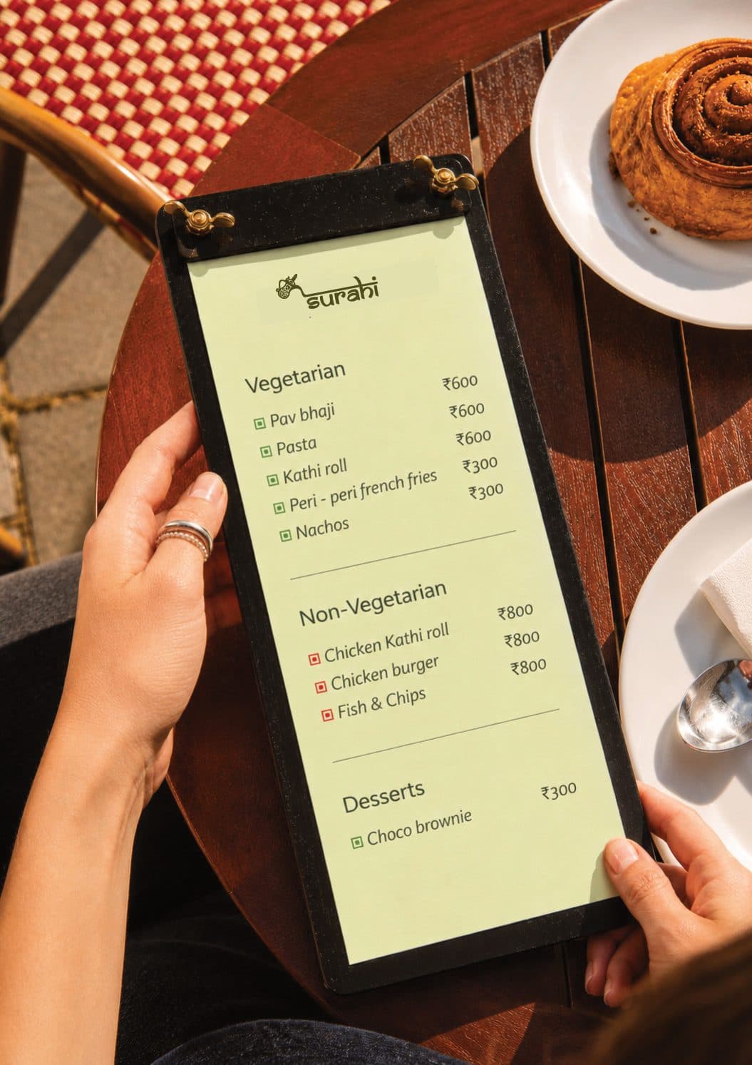 Hands holding the Surahi snack menu at a café table