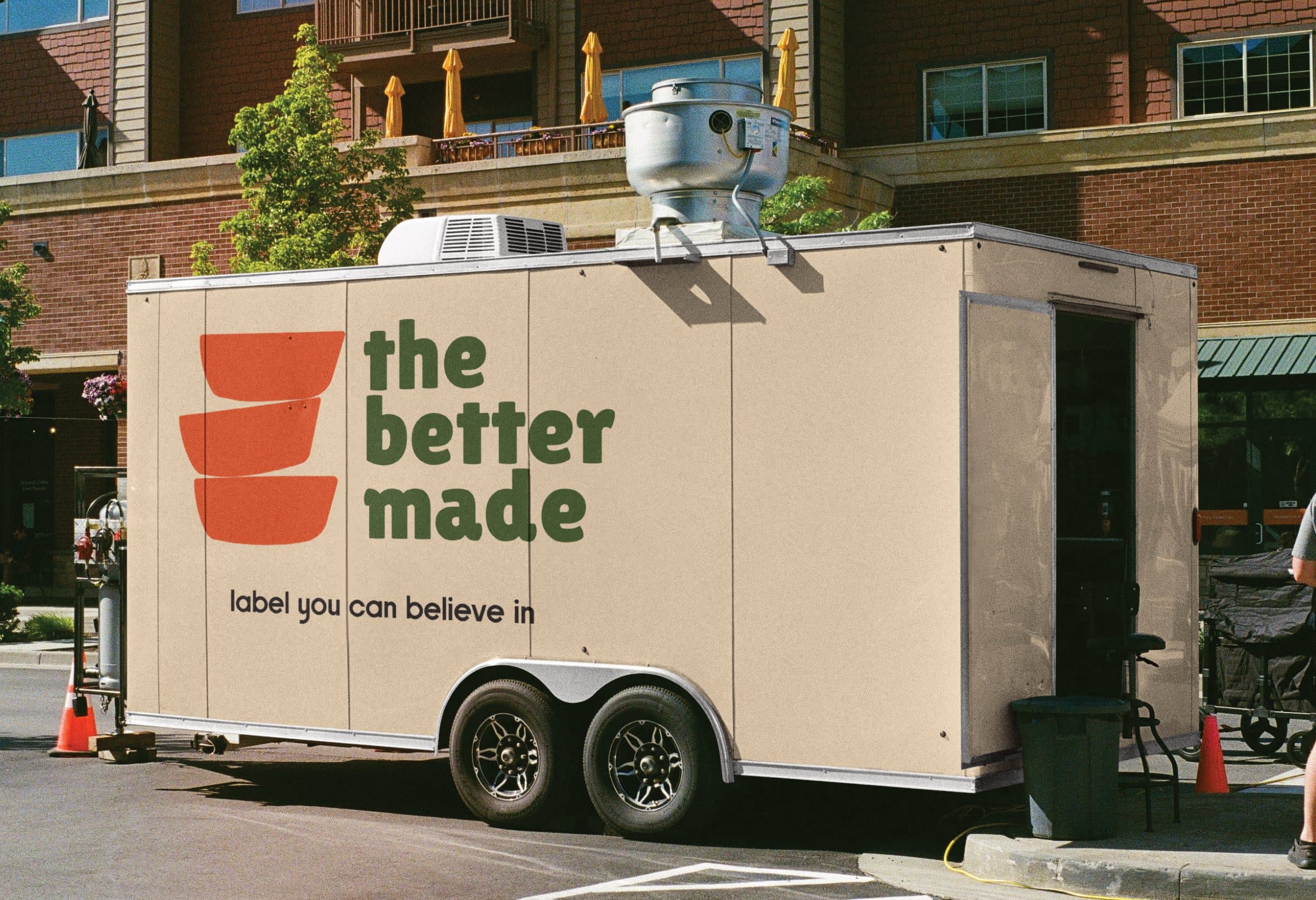 A beige food trailer carrying the Better Made logo and the line “label you can believe in”, parked outside a brick building